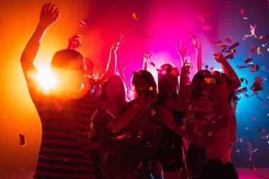 Silüet giymiş bir kalabalık ellerini neon ışıklı arka planda dans pistine kaldırıyor.
