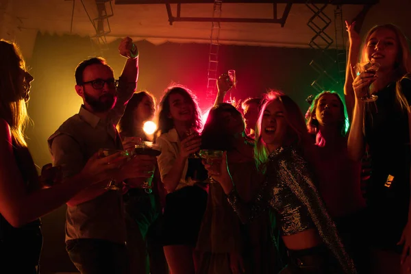 Silüet giymiş bir kalabalık ellerini neon ışıklı arka planda dans pistine kaldırıyor. — Stok fotoğraf