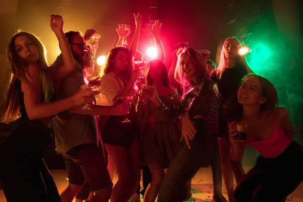 A crowd of people in silhouette raises their hands on dancefloor on neon light background — Stock Photo, Image