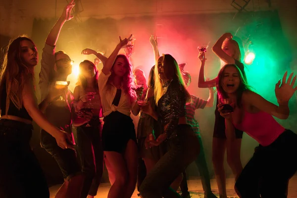 Une foule de gens en silhouette lève les mains sur la piste de danse sur fond clair néon — Photo