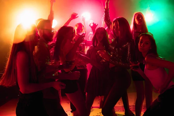 A crowd of people in silhouette raises their hands on dancefloor on neon light background — Stock Photo, Image