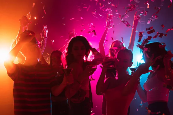 Uma multidão de pessoas em silhueta levanta as mãos na pista de dança no fundo de luz de néon — Fotografia de Stock