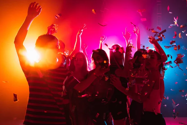 A crowd of people in silhouette raises their hands on dancefloor on neon light background — Stock Photo, Image
