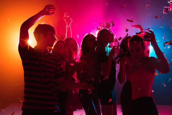 Una folla di persone in silhouette alza le mani sulla pista da ballo su sfondo luce al neon — Foto Stock