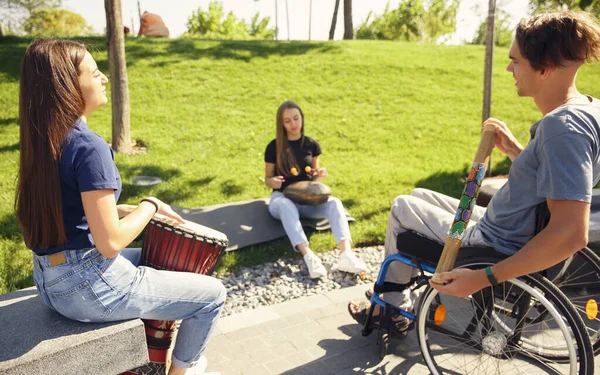 Šťastný handicapovaný muž na invalidním vozíku tráví čas s přáteli hraní živé instrumentální hudby venku — Stock fotografie