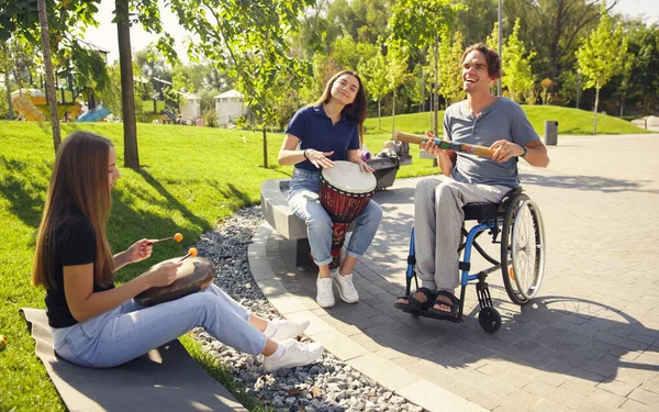 Šťastný handicapovaný muž na invalidním vozíku tráví čas s přáteli hraní živé instrumentální hudby venku — Stock fotografie