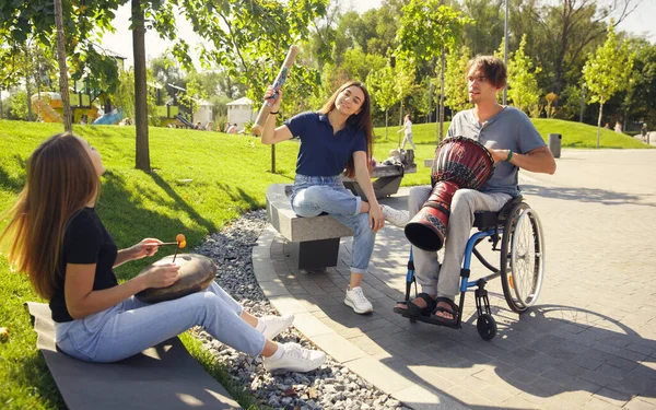 Šťastný handicapovaný muž na invalidním vozíku tráví čas s přáteli hraní živé instrumentální hudby venku — Stock fotografie