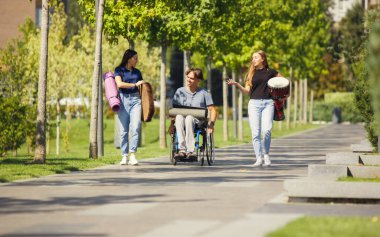 Tekerlekli sandalyede arkadaşlarıyla dışarıda enstrümantal müzik çalarak vakit geçiren mutlu engelli adam.