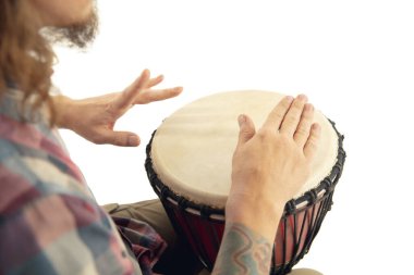 Adam etnik davul darbuka perküsyonu çalıyor, beyaz stüdyo arka planında izole edilmiş müzisyeni kapatıyor.
