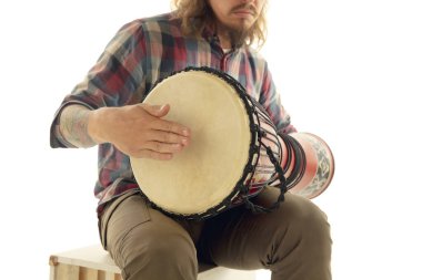 Adam etnik davul darbuka perküsyonu çalıyor, beyaz stüdyo arka planında izole edilmiş müzisyeni kapatıyor.