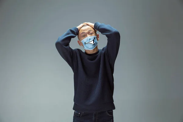 Retrato de un joven con emoción en su máscara protectora aislada en el fondo del estudio. Hermoso modelo masculino, expresión divertida — Foto de Stock