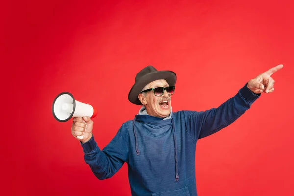 Старший чоловік у стильному окулярах та капелюсі ізольований на червоному тлі. Технічна та радісна концепція способу життя літніх людей — стокове фото