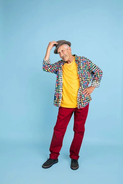 Homem hipster sênior em chapéu elegante isolado em fundo azul. Conceito de tecnologia e estilo de vida idoso alegre — Fotografia de Stock