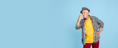 Şık şapkalı kıdemli hippi adam mavi arka planda izole edilmiş. Teknolojik ve neşeli yaşlı yaşam tarzı konsepti