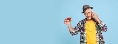 Şık şapkalı kıdemli hippi adam mavi arka planda izole edilmiş. Teknolojik ve neşeli yaşlı yaşam tarzı konsepti