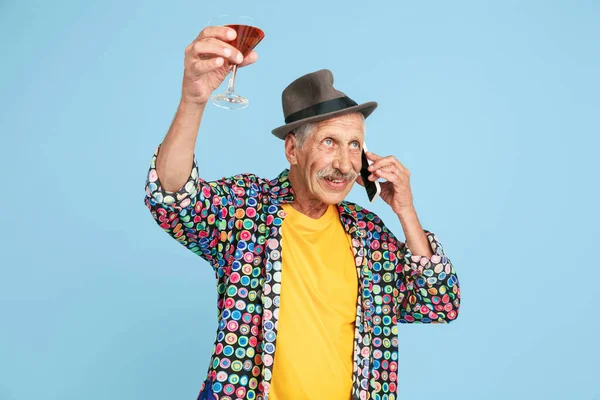 Homem hipster sênior em chapéu elegante isolado em fundo azul. Conceito de tecnologia e estilo de vida idoso alegre — Fotografia de Stock