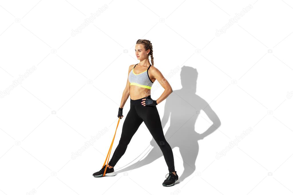 Beautiful young female athlete practicing on white studio background with shadows