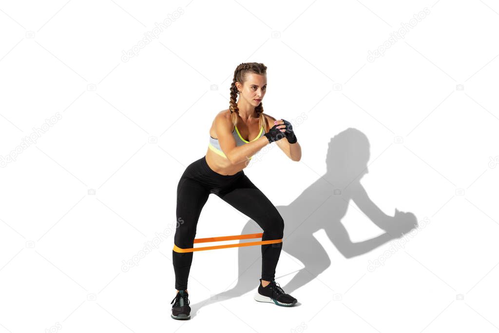 Beautiful young female athlete practicing on white studio background with shadows