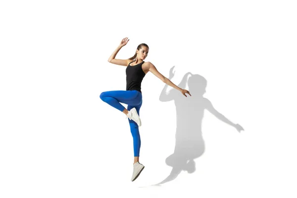 Bella giovane atleta donna che si estende su sfondo bianco studio con ombre — Foto Stock