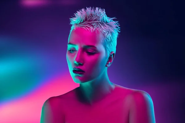 stock image Portrait of female fashion model in neon light on dark studio background.