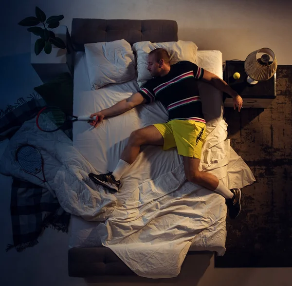 Vista superior de un joven tenista profesional durmiendo en su dormitorio en ropa deportiva con raqueta —  Fotos de Stock