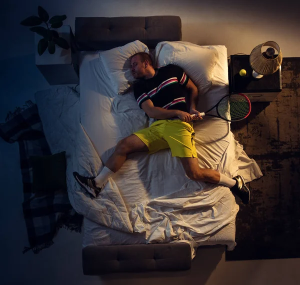Vista superior de un joven tenista profesional durmiendo en su dormitorio en ropa deportiva con raqueta — Foto de Stock