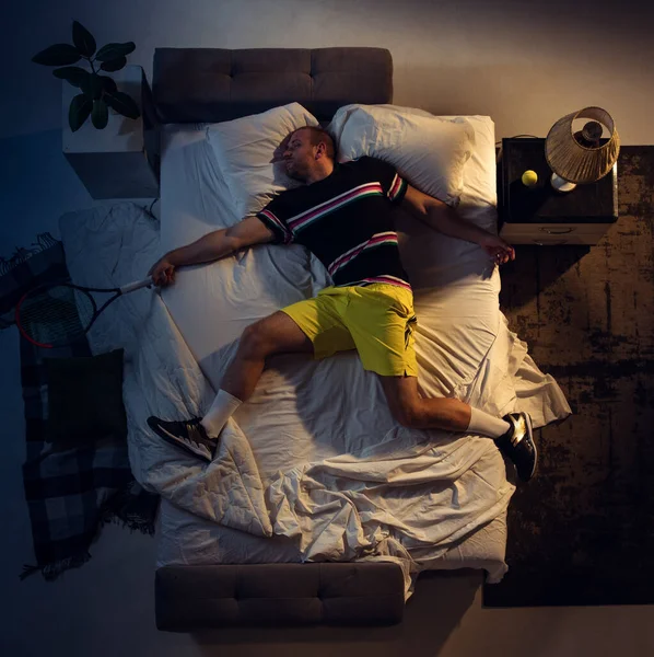 Vista superior de un joven tenista profesional durmiendo en su dormitorio en ropa deportiva con raqueta —  Fotos de Stock