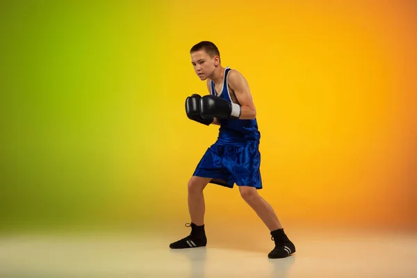 Boxeador adolescente contra gradiente neón fondo del estudio en movimiento de patadas, boxeo — Foto de Stock