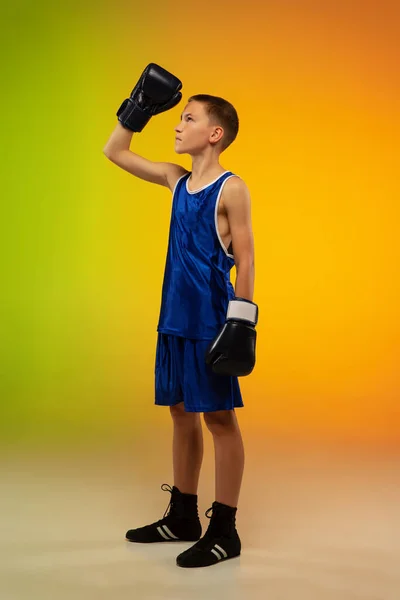 Nastoletni bokser na tle gradientowego neonowego studia w ruchu kopania, boksu — Zdjęcie stockowe