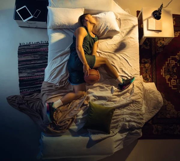 Vista superior de un joven jugador de baloncesto profesional durmiendo en su dormitorio en ropa deportiva con pelota —  Fotos de Stock