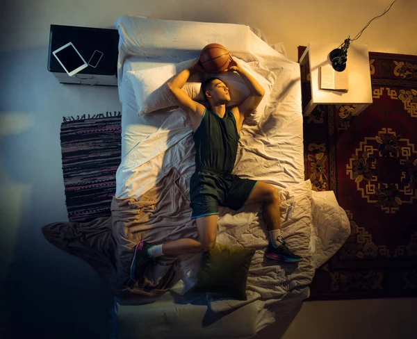 Vista superior de un joven jugador de baloncesto profesional durmiendo en su dormitorio en ropa deportiva con pelota —  Fotos de Stock