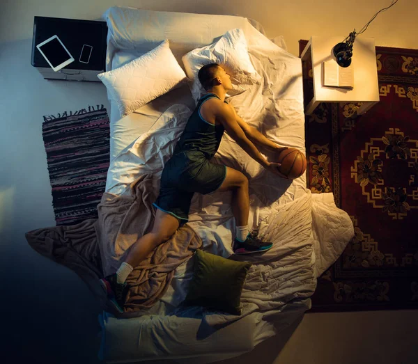 Vista superior de un joven jugador de baloncesto profesional durmiendo en su dormitorio en ropa deportiva con pelota —  Fotos de Stock