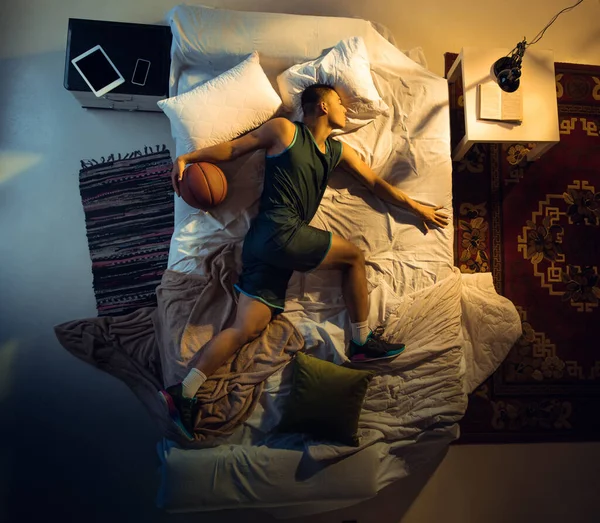 Vista superior de un joven jugador de baloncesto profesional durmiendo en su dormitorio en ropa deportiva con pelota —  Fotos de Stock