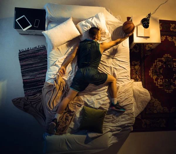 Vista superior de un joven jugador de baloncesto profesional durmiendo en su dormitorio en ropa deportiva con pelota —  Fotos de Stock