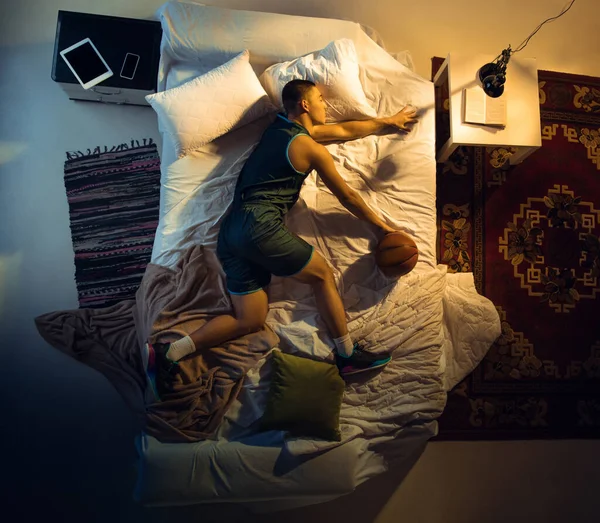 Vista superior de un joven jugador de baloncesto profesional durmiendo en su dormitorio en ropa deportiva con pelota —  Fotos de Stock