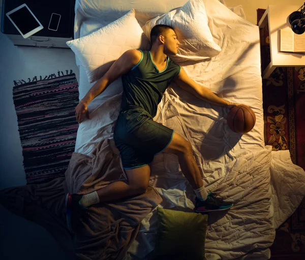 Vista superior de un joven jugador de baloncesto profesional durmiendo en su dormitorio en ropa deportiva con pelota —  Fotos de Stock