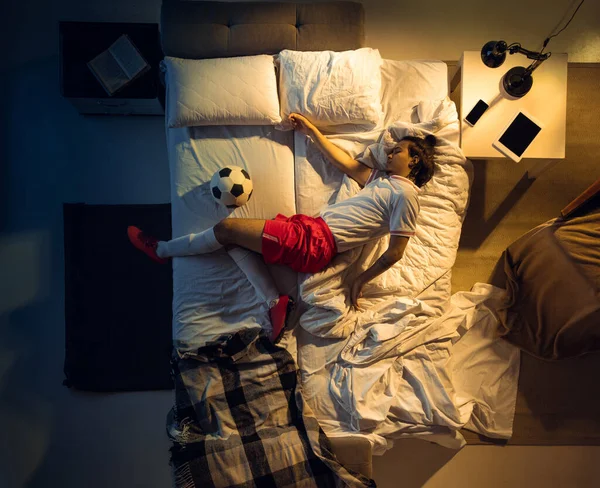Ovanifrån av ung professionell fotboll, fotbollsspelare sover i sitt sovrum i sportkläder med boll — Stockfoto