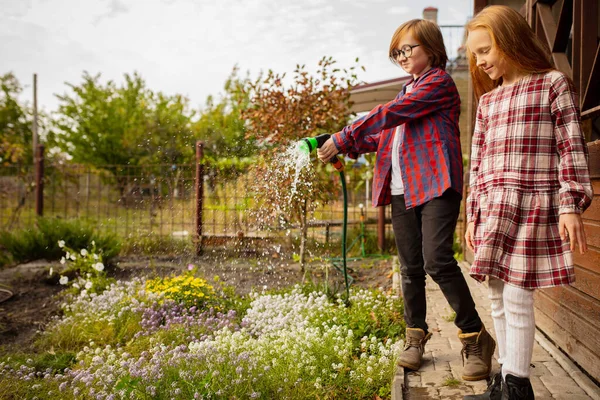 Glückliches Geschwisterpaar gießt gemeinsam Pflanzen im Garten — Stockfoto