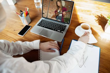 Genç doktor internette dizüstü bilgisayarla çalışıyor, gülümseyen şarkıcıyla online müzik konsepti izliyor.