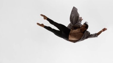 Erkek dansçı, odaklanmış bakışları ve duygusal tutumuyla paltoyla yatay olarak süzülüyor. Yayın erkek giyim, performans sanatı, psikolojik farkındalık ve somatik denge kavramı.