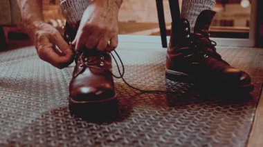 Metal zemine sağlam kahverengi deri çizmeler bağlayan yüzü olmayan adam. Açık hava yaşam tarzı, iş kıyafeti hazırlığı, esneklik, günlük rutin ve pratik stil kavramı.