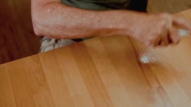 Evdeki temizlik ürünleri ve kumaşlarla ahşap yüzeyi silen bir adam. Ev işleri, hijyen, rutin bakım, kişisel sorumluluk ve yaşam tarzı bakımı kavramı.