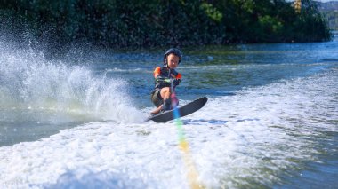 Siyah kasklı bir çocuk su kayağı yaparken öne eğiliyor. Denge, kararlılık, adrenalin, duygusal güç ve açık hava yaz yarışması kavramı.