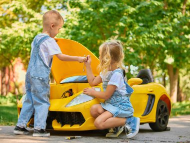 Çocuklar dışarıda araç gereçlerle ve takım çalışmasıyla sarı oyuncak araba tamir ediyorlar. Sosyal iyilik kavramı, çocukluk işbirliği, hayal gücü, oyun temelli öğrenme ve açık hava yaratıcılığı.