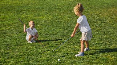 Çocuklar yeşil çimlerde gülücükler ve eğlence enerjisiyle golf oynuyorlar. Takım çalışması, çocukluk sevinci, açık hava eğitimi, odaklanma ve sağlıklı yaşam tarzı kavramı..