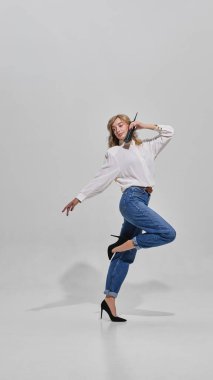 Elinde retro telefonla dans eden bir kadın bluz kotu ve topuklu ayakkabı giyiyor. Yaratıcılık, moda hareketi, denge, yaşam tarzı ve tarz güveni kavramı.