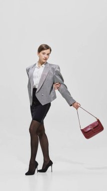 Kırmızı çantalı, gümüş ceketli ve siyah etekli şık bir kadın poz veriyor. İktidar giyimi, kurumsal moda, bağımsızlık, cesur hırs ve güven kavramı.