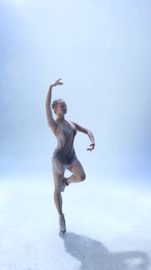 Dişi patenci beyaz sahnede tek bacağının üzerinde zarif bir şekilde dengede duruyor. Fitness disiplini, kültürel sanat, yaşam tarzı zarafeti ve dışavurumcu hareket kavramı.