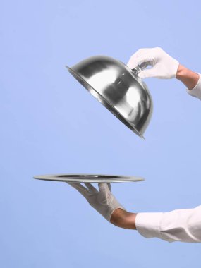 Eller mavi arka plandaki tepsiden gümüş saati kaldırıyor. Gurme yemeklerini tanıtma, iş ürünlerini sunma, yemek servisi ve zarif yemek servisi kavramı. Reklamlar için negatif alan