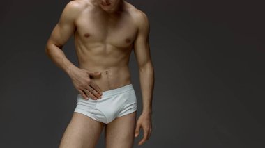 Beyaz iç çamaşırlı erkek model karnına dokunurken kendine güvenen duruşunda duruyor. İç çamaşırı reklamı, sağlık kampanyaları, anatomi eğitimi ve fitness markalaşması kavramı.